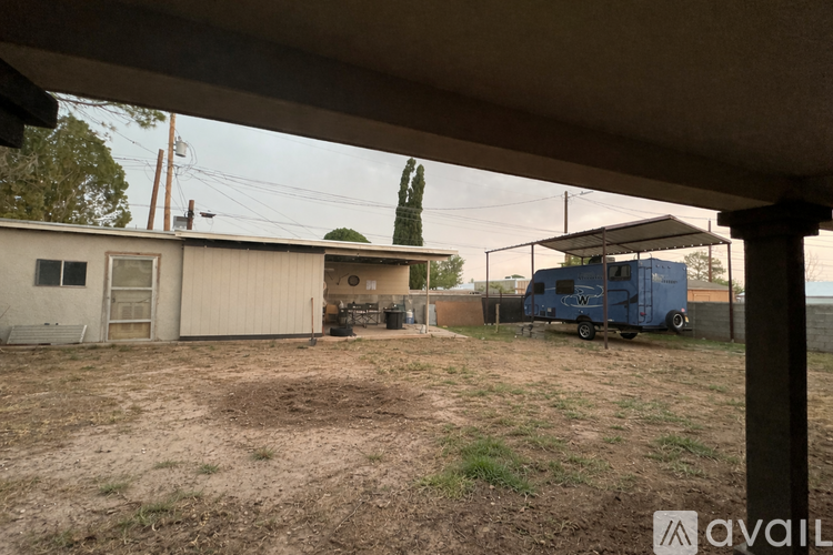 A blue trailer is parked in a lot with a building and trees in the background.