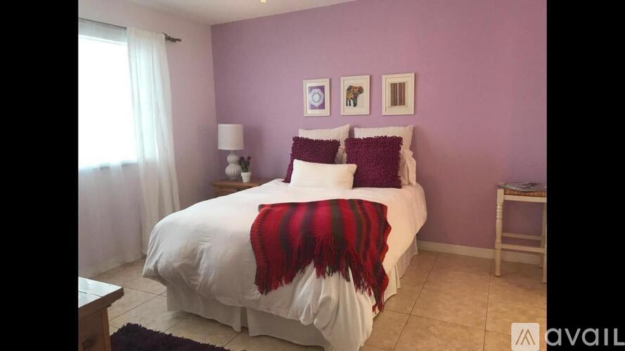 A bedroom with a bed covered in a white sheet and a red and black striped blanket.