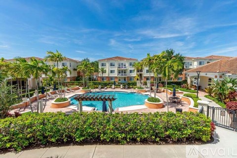 A large swimming pool surrounded by a green hedge and palm trees.