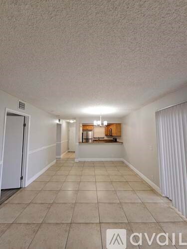 A spacious room with tiled flooring and a small kitchenette in the distance.