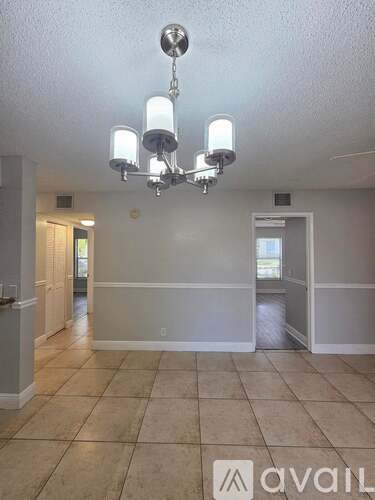 A chandelier hangs over a tiled floor in a room with white walls.