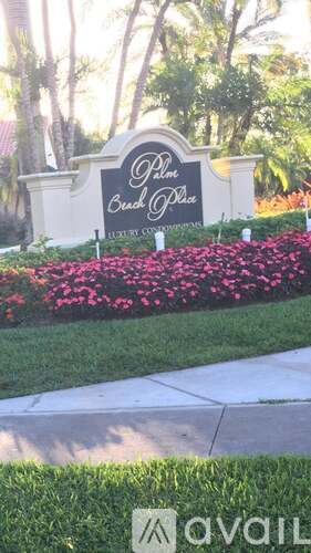 A sign that says "Palm Beach Place" in front of some flowers.