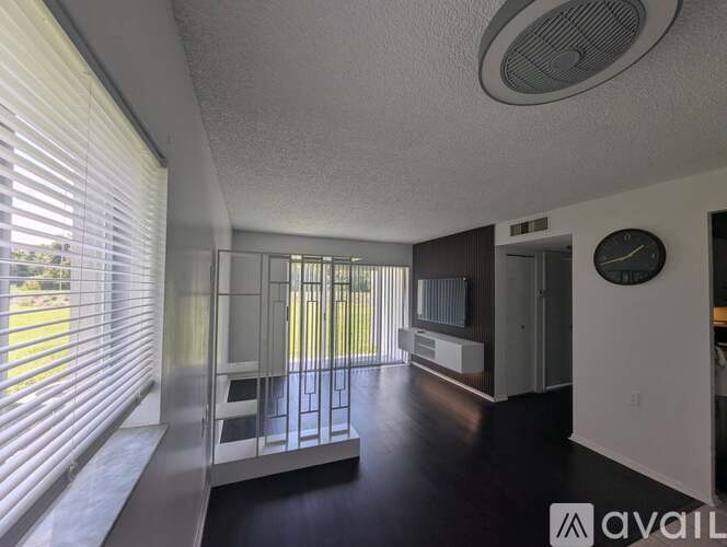 A living room with a television, a window with blinds, and a clock on the wall.