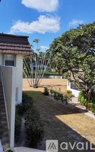 A house with a brown roof and a white wall is surrounded by greenery.