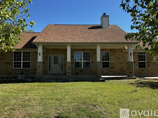 A house with a brown roof and a chimney is surrounded by a grassy lawn.