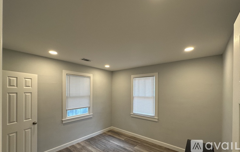 A room with a door, two windows, and a wooden floor.