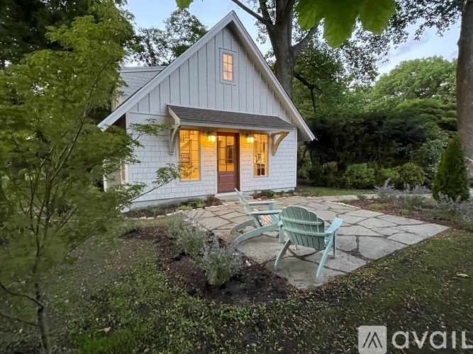 A small white house with a grey roof and a green chair in front of it.