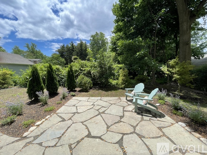 A stone patio with two chairs and a backdrop of trees.