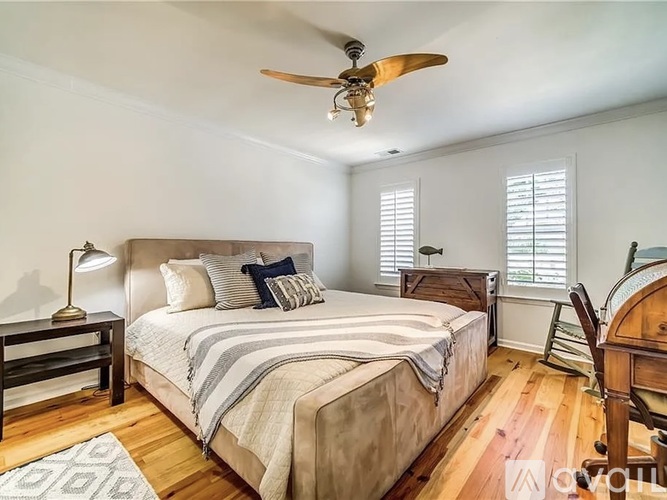 A bedroom with a bed, a ceiling fan, and a wooden floor.