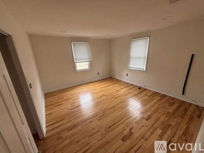 A room with wooden flooring and two windows with blinds.