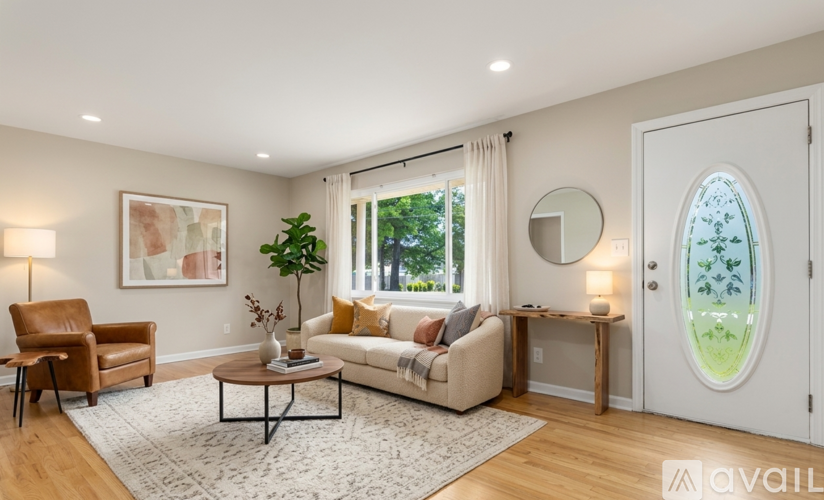 A living room with a brown leather chair, a white sofa, a coffee table, and a large window with a view of trees.