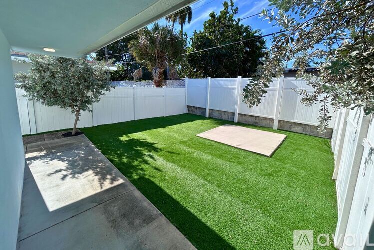 A backyard with a white fence and a green lawn.