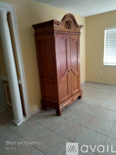 A wooden armoire stands in a room with a white column and a window.