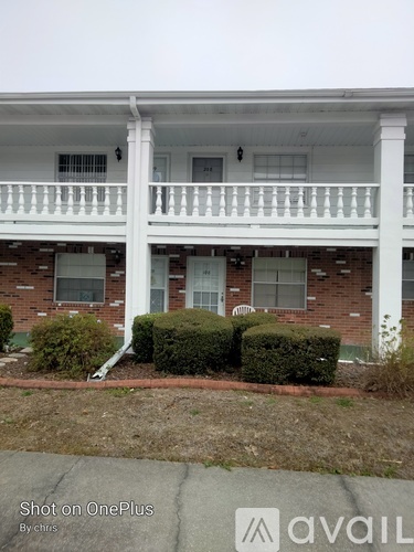A white two-story building with a balcony and a brick facade.