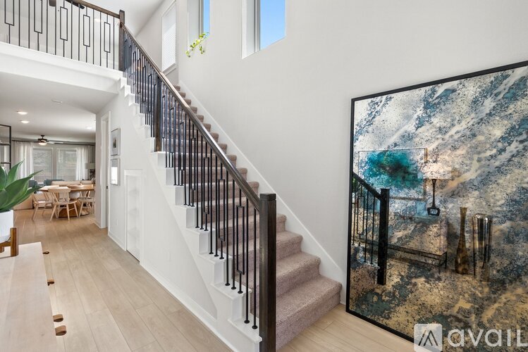 A painting of a beach scene is displayed on a wall in a spacious room with a staircase.