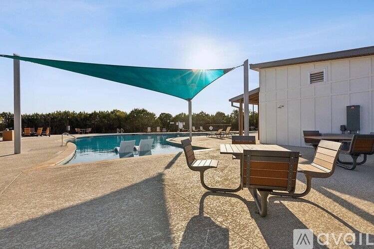 A sunny day at the pool with a green shade sail and a wooden bench.