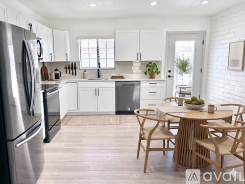 A kitchen with a refrigerator on the left and a dining table with chairs in the middle.