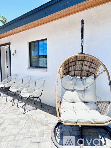 A white chair with a cane back and a cushion is in front of a white building with a blue roof.