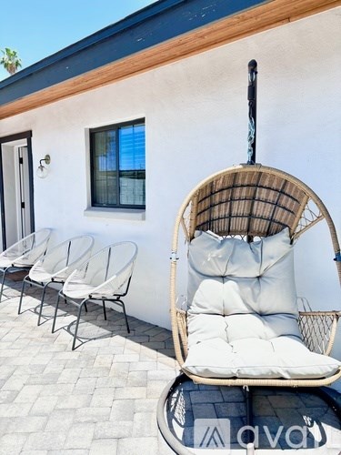 A white chair with a cane back and a cushion is in front of a white building with a blue roof.
