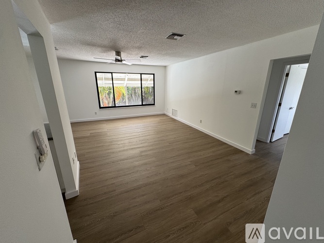 A spacious room with wooden flooring and a window with blinds.