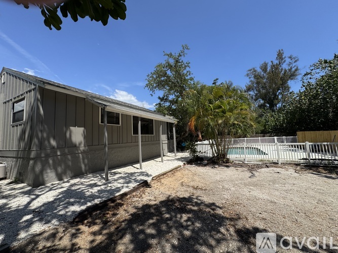 A grey house with a white fence and trees in the background.