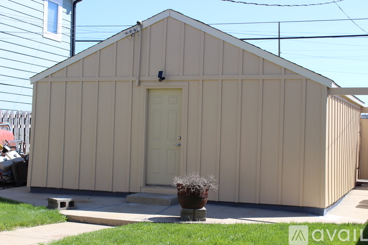 A small beige building with a white door and a small plant in front.