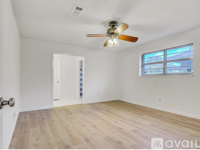 A room with a ceiling fan and a window with a view of trees.