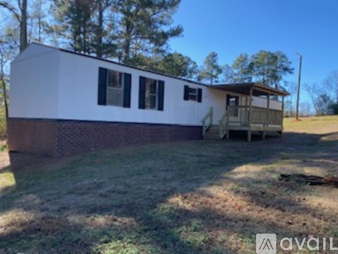A white mobile home with a brown brick foundation sits in a grassy field.