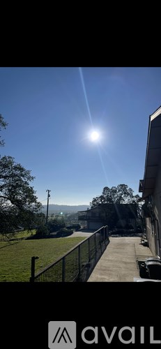 A bright sun shines in a clear blue sky over a residential area.