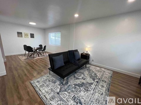 A living room with a black couch and a rug.