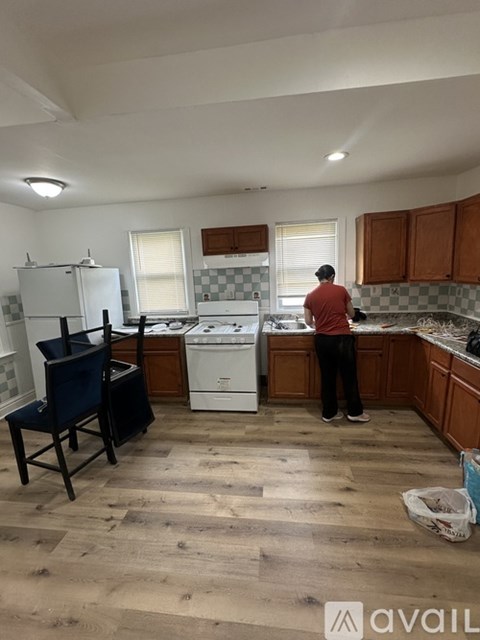 A man is standing in a kitchen with wooden floors and white appliances.