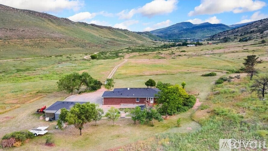 A house with a red roof is surrounded by greenery and a dirt road.