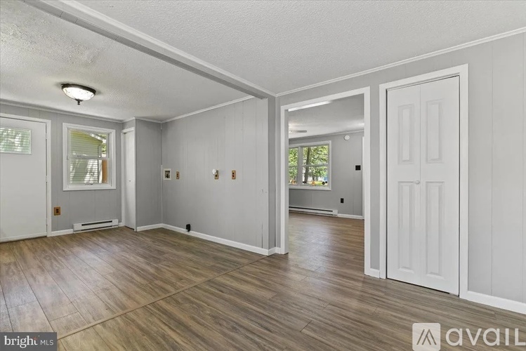 A room with white walls and wooden flooring, with a door on the right side.