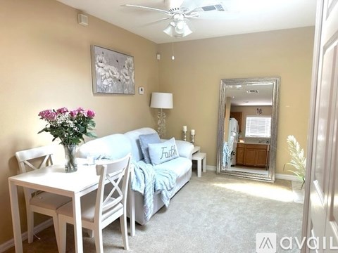 A living room with a white couch, a table with a vase of flowers, and a mirror on the wall.