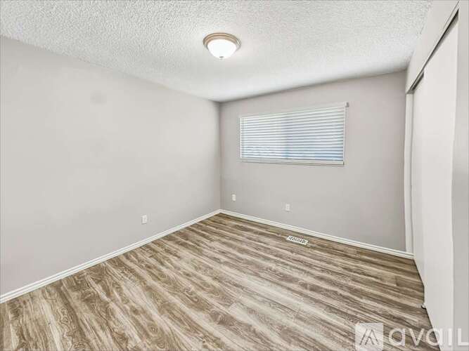 A room with wooden flooring and a window with blinds.