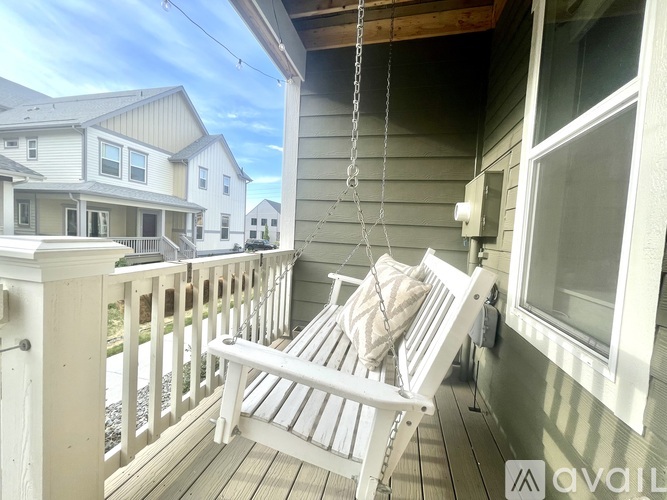 A white wooden porch swing hangs from a chain on a wooden deck.