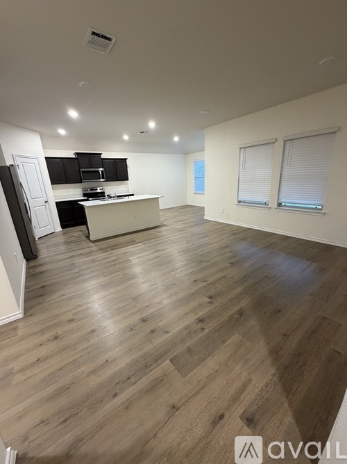 A spacious room with wooden flooring and a kitchen area with a stove and cabinets.