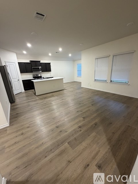 A spacious room with wooden flooring and a kitchen area with a stove and cabinets.
