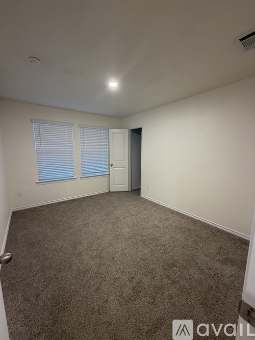 A carpeted room with a door and a window with blinds.