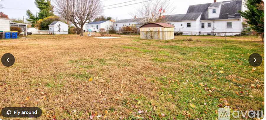 A grassy field with a white house and a shed in the background.