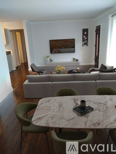 A living room with a grey couch, a marble table and green chairs.