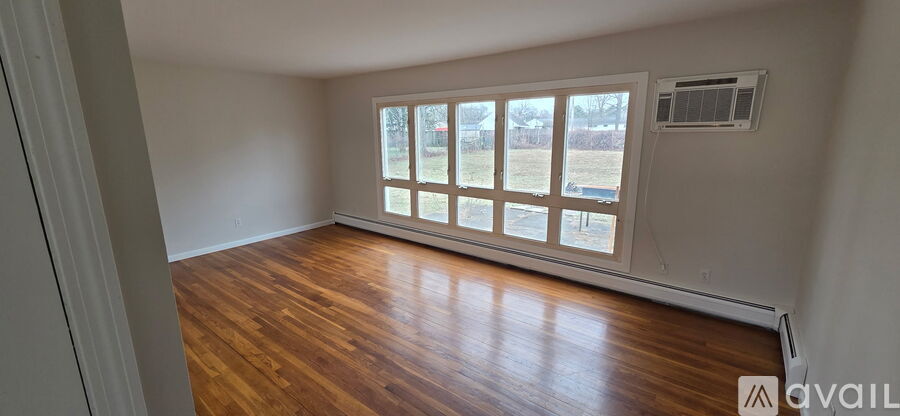 A room with wooden floors and a large window with a view of a yard.