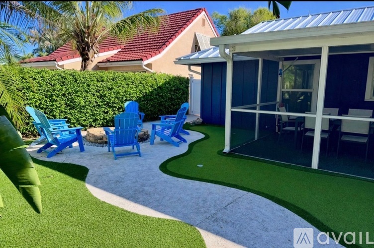 A patio with blue chairs and a white table is surrounded by a green lawn.
