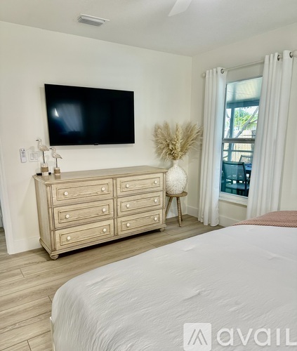 A bedroom with a large bed, a TV, and a dresser with a vase on top.