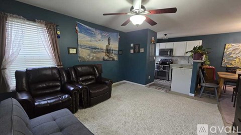 A living room with a black leather couch and a ceiling fan.