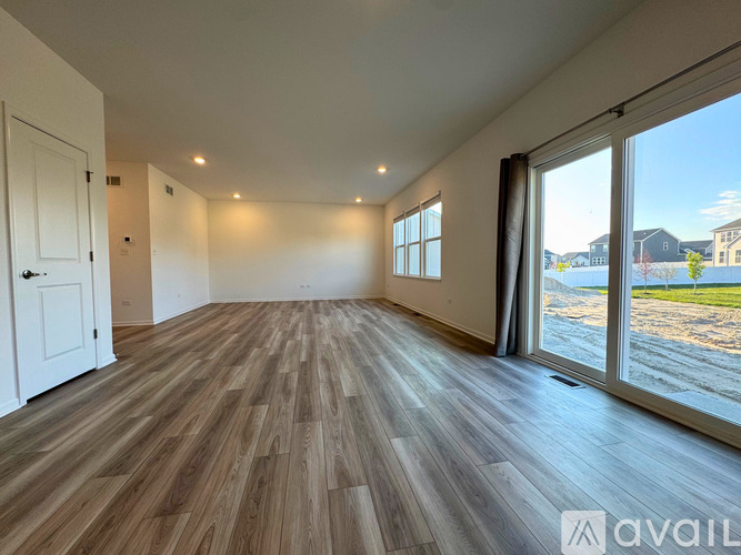 A spacious room with wooden flooring and large windows overlooking a residential area.