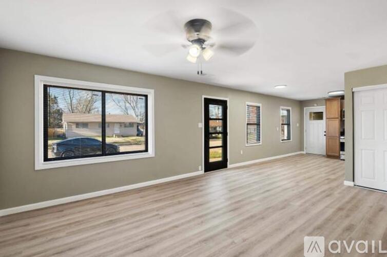 A spacious room with a ceiling fan and a large window overlooking a car and a house.
