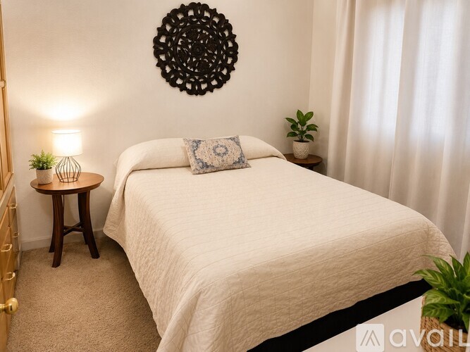 A bedroom with a bed, a side table with a lamp, and a wall hanging.