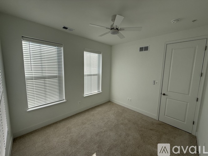 A room with a carpeted floor, a ceiling fan, and a door.