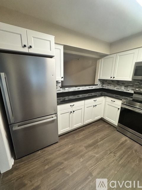 A kitchen with a stainless steel refrigerator and wooden flooring.
